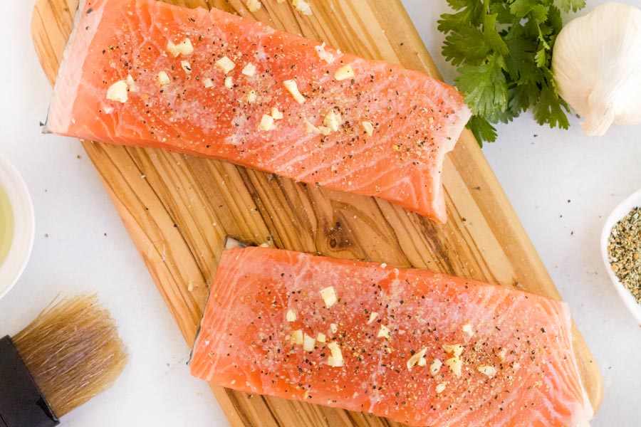 salmon on a cutting board next to a basting brush and garlic