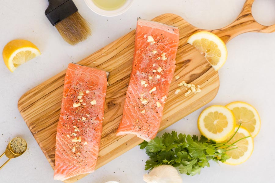 salmon fillets on a wooden cutting board next to lemon slices and parsley