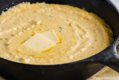 a cast iron skillet with creamy cheese grits in it topped with melted butter