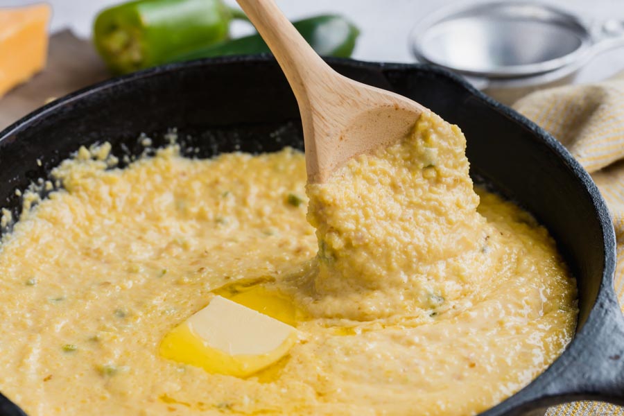 keto grits dripping down a wooden spoon over a skillet pan