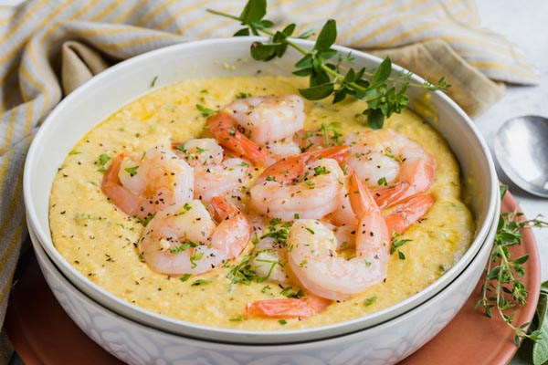 Keto grits in a white bowl with cooked shrimp on the surface