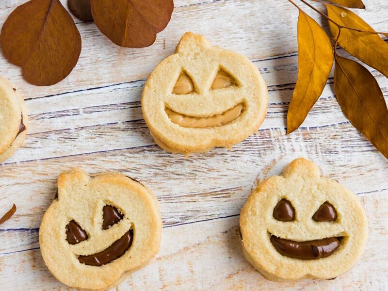 three pumpkin sandwich cookies with dries leaves above