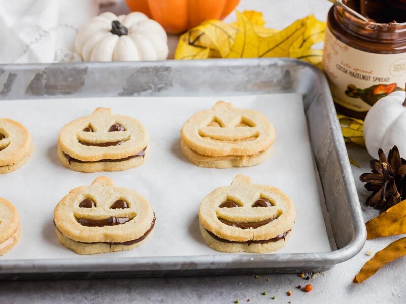 chocolate hazelnut spread filled pumpkin cookies on a baking tray next to pumpkins and leaves