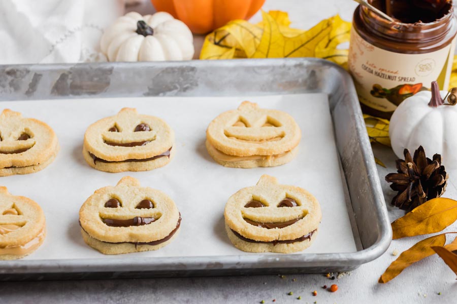 chocolate hazelnut spread filled pumpkin cookies on a baking tray next to pumpkins and leaves