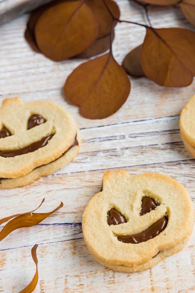 a chocolate faced jack o lantern cookie next to another cookie with dried leaves around