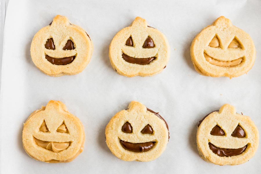six jack o lantern shaped cookies in a row filled with melted dark chocolate and white chocolate