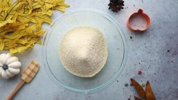 a bowl with dry ingredients inside next to a spatula and yellow leaves