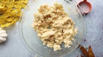 cookie dough in a bowl next to dried leaves and a cookie cutter