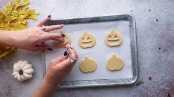 cutting a jack o lantern face out of a cookie with a knife