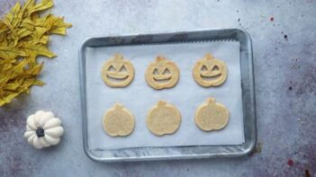 a baking tray with three cookies with a jack o lantern face and three whole pumpkin cookies on it