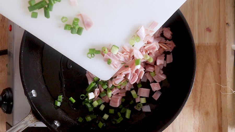 adding sliced ham and sliced green onion to a skillet