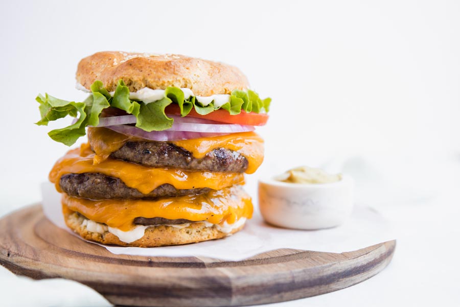 a platter with a big hamburger on it with three patties lettuce and tomatoe