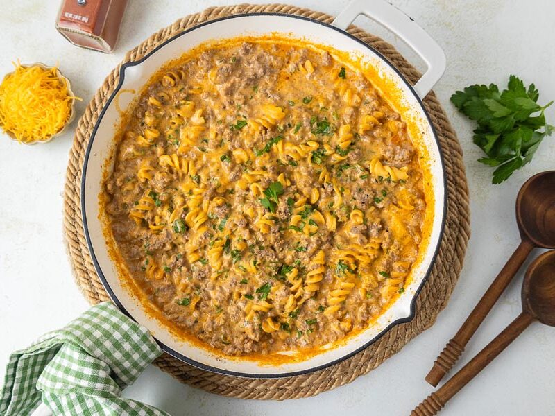Cheesy hamburger casserole in a skillet next to serving spoons and shredded cheese.