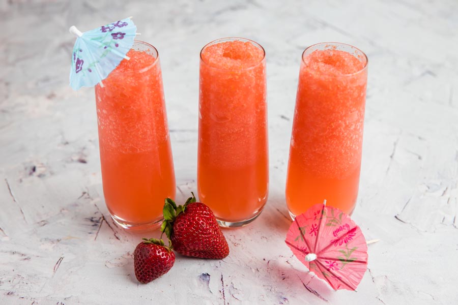 two small glass of a frozen sugar free strawberry cocktail with berries on the side and umbrellas in the drink