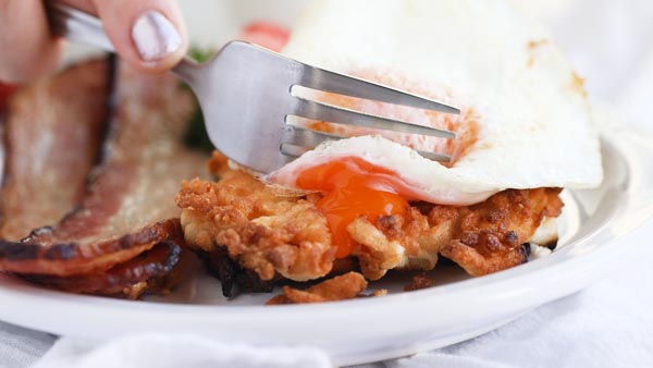 cutting an egg with a fork over a hashbrown