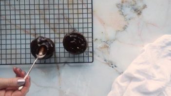 covering a cupcake with chocolate ganache on a wire rack