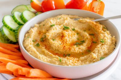 A bowl of creamy keto hummus in a bowl next to fresh vegetables.