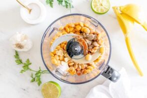 A food processor with whole lupini beans and other hummus ingredients inside it.