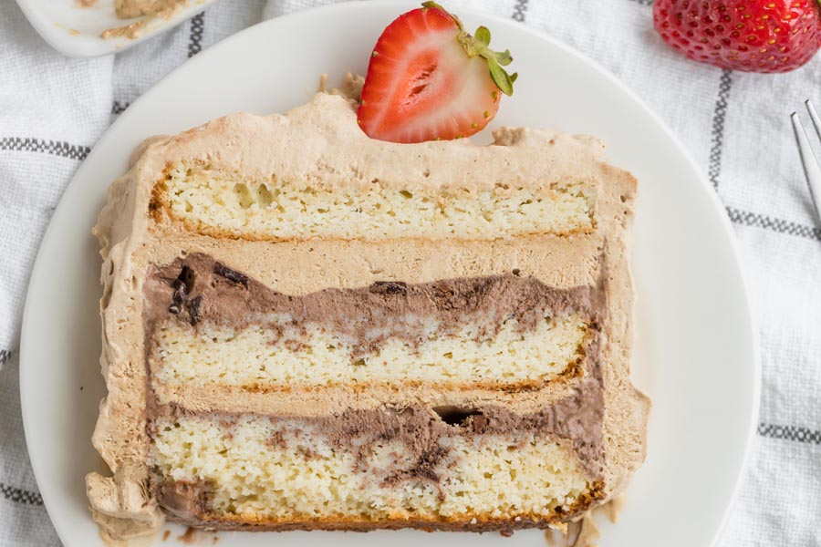 a slice of ice cream cake with layers of white cake, chocolate ice cream and chocolate whipped topping and topped with a sliced straweberry