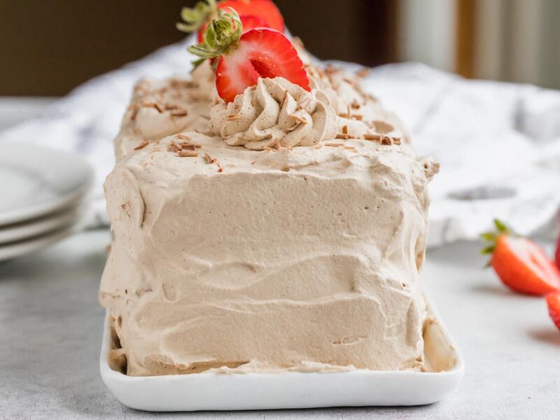 a loaf cake covered in chocolate whipped topping and sliced strawberries