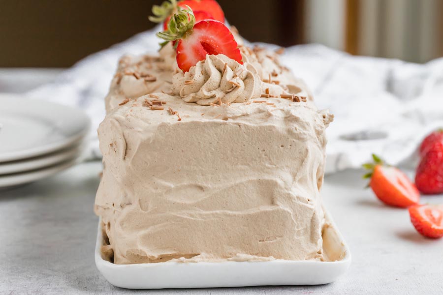 a loaf cake covered in chocolate whipped topping and sliced strawberries