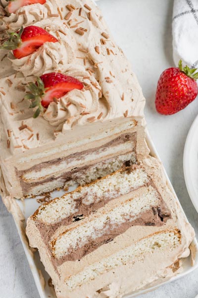 a slice of ice cream cake laying in front of a whole cake with a strawberry near by