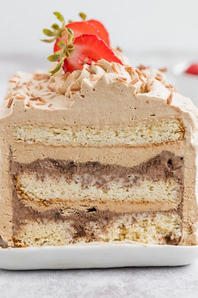 a sliced cake on a dish showing layers of cake and ice cream and covered in a light chocolate frosting