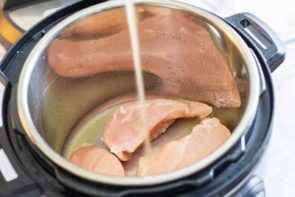 pouring chicken broth into the instant pot with breast meat in it