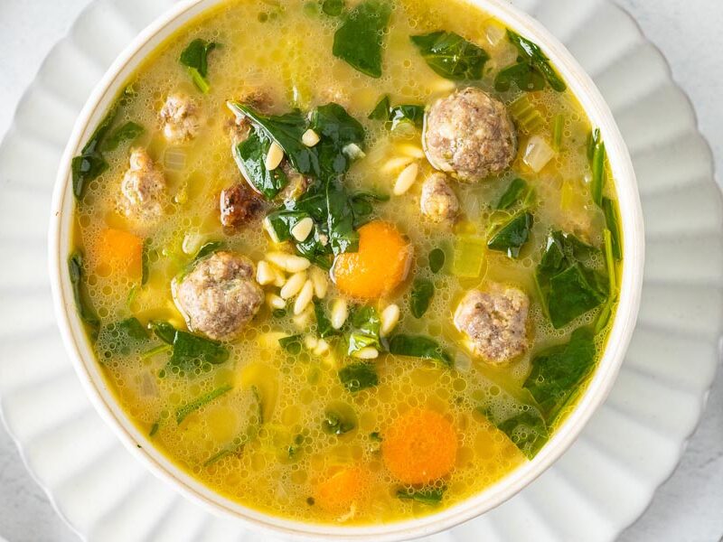 Looking down into a savory bowl of Italian wedding soup with meatballs and orzo pasta.