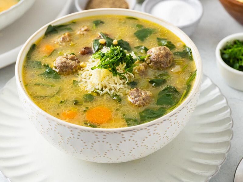 A bowl of meatball soup topped with parmesan cheese and parsely.