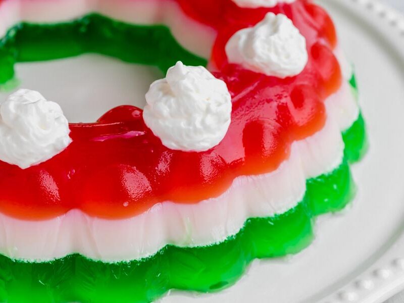 A layered jello mold on a platter topped with whipped cream.