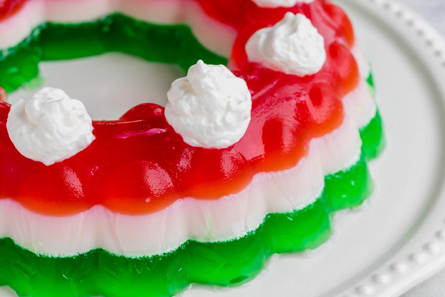 A layered jello mold on a platter topped with whipped cream.