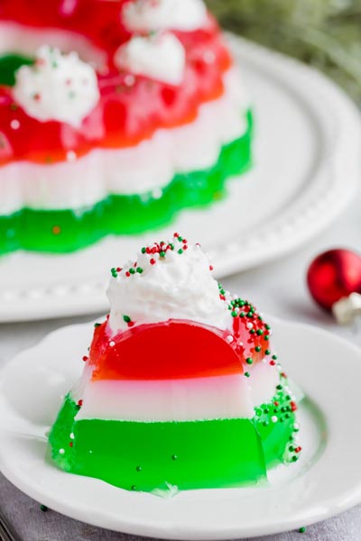 A slice of layered jello on a plate with layers of strawberry, marshmallow and lime.