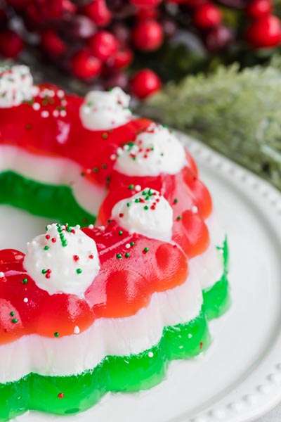 A jello mold on a plate with red, white and green layers and topped with dollops of whipped cream.