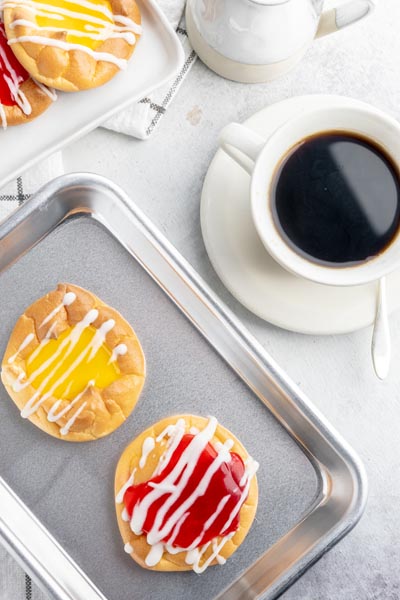 looking down to see a cup of black coffee and a baking tray with lemon and cherry danishes on it