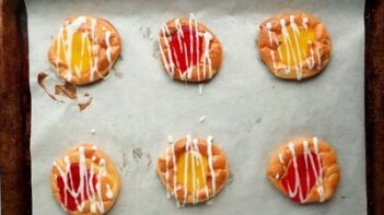 a baking tray with cherry and lemon danishes on it topped with icing