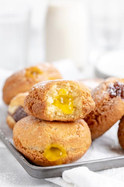 a baking tray with lemon and strawberry filled donuts with the top donut a bite out of it