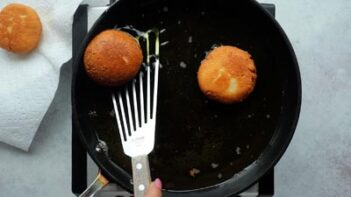 a slotted spatula scooping up a round donut from a skillet with oil