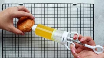 filling a donut with lemon jelly with an injector over a wire rack