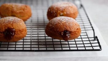 four donuts filled with jelly on a wire baking rack and dusted with powdered sugar