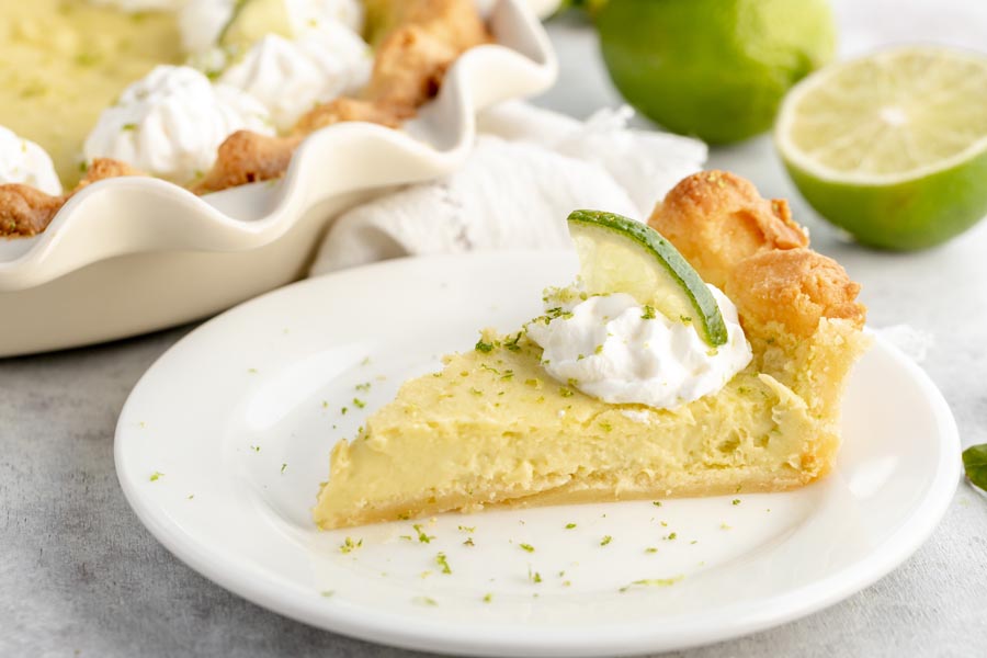 a slice of silky cream pie on a small white plate with green lime zest sprinkled around