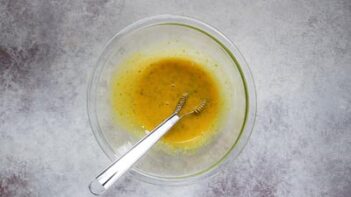 a whisk sitting in a bowl of whisked egg yolks and lime zest