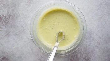 light green pie filling in a clear bowl with a whisk sitting above