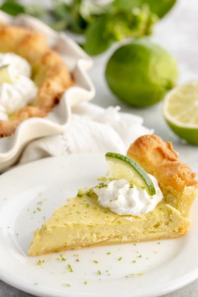 a slice of key lime pie on a white plate with a dollop of whipped cream and lime slice on top