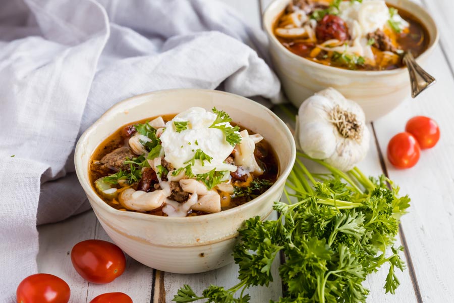 bowls of instant pot lasagna soup with tomatoes and garlic nearby