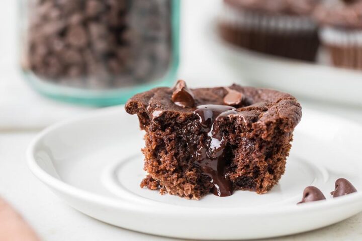A rich chocolate lava cake muffin with a molten center oozing out, sitting on a white plate.