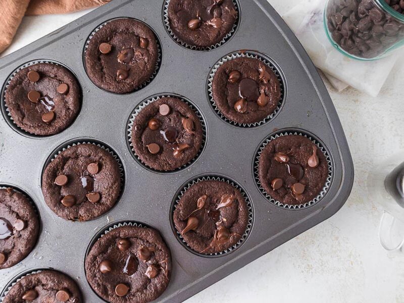 A full tray of freshly baked keto lava cake muffins topped with melted chocolate chips.