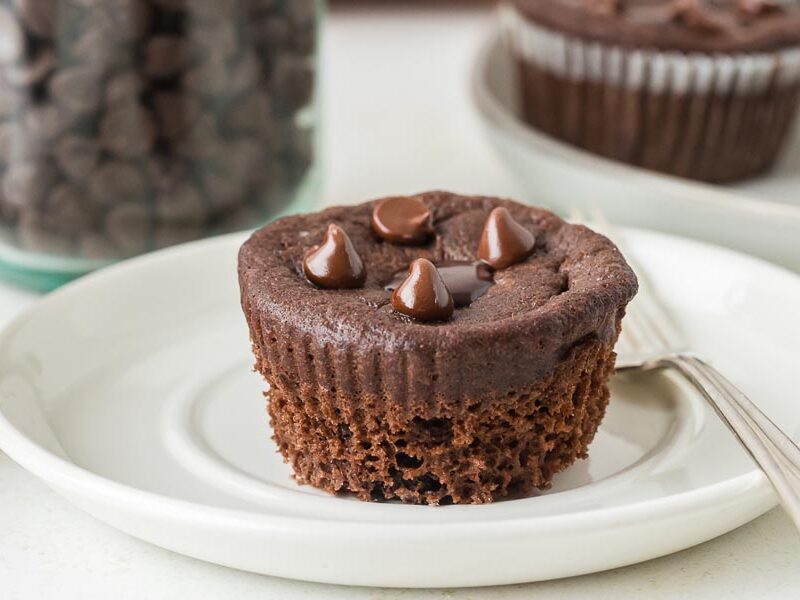 A single keto chocolate muffin topped with glossy chocolate chips, displayed on a white plate.