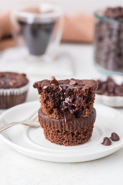 Two stacked keto lava cake muffins on a plate, with the top muffin bitten to reveal its gooey chocolate center.