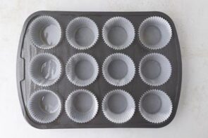 A 12-cup muffin pan lined with white cupcake liners and lightly sprayed with oil, ready for batter.